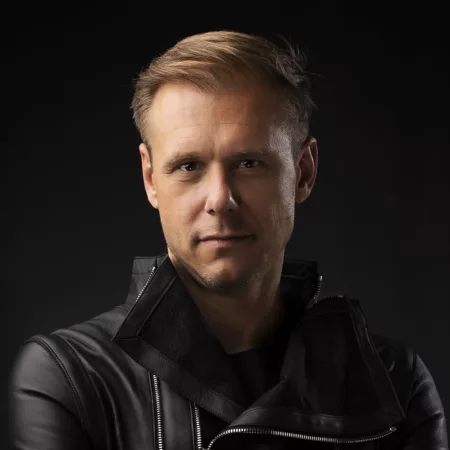 Portrait d'Armin van Buuren, vêtu d'une veste en cuir noir, avec un fond sombre.