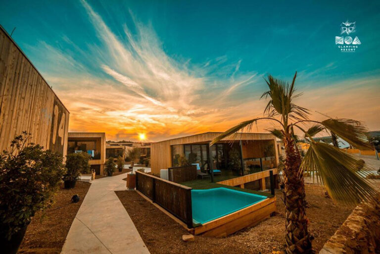 Vue du Noa Glamping Resort au coucher du soleil, montrant des bungalows modernes avec piscines privées.