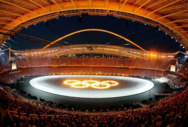 Stade olympique bondé lors des Jeux Olympiques d'Athènes 2004, avec les anneaux olympiques illuminés au centre de l'arène.