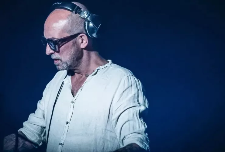 DJ Tomcraft se produisant sur scène, portant une chemise blanche, un casque et des lunettes, concentré sur son équipement.