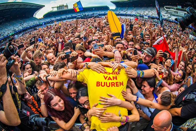 Armin van Buuren, vêtu d'un maillot jaune avec son nom, entouré et acclamé par une foule enthousiaste lors du festival Untold 2018.