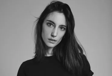 Portrait en noir et blanc d'Amelie Lens, DJ et productrice belge, avec un regard intense et des cheveux mi-longs, vêtue d'un haut noir sur fond neutre.