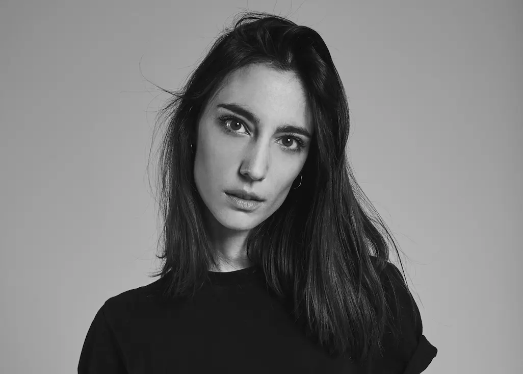 Portrait en noir et blanc d'Amelie Lens, DJ et productrice belge, avec un regard intense et des cheveux mi-longs, vêtue d'un haut noir sur fond neutre.